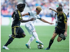 Erik Hurtado of the Vancouver Whitecaps moves the ball past Columbus Crew's Lalas Abubakar, left, and Wil Trapp during the second half of Saturday's Major League Soccer game in Vancouver. The Caps scored a late goal to salvage a 2-2 draw.