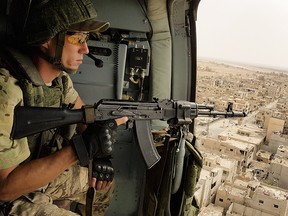 In this Friday, Sept. 15, 2017 photo a Russian soldier guards as a military helicopter flies over Palmyra, Syria. Government troops and their allies intensified an offensive Friday against Islamic State militants in central Syria, trying to consolidate their control on the area.