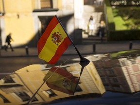 People walk past by a car with a Spanish flag attached on top in Madrid, Tuesday, Oct. 24, 2017. Spain's Senate is expected to greenlight Rajoy's plan on Friday, triggering previously untapped constitutional powers to act against regional leaders disobeying the country's top law. (AP Photo/Francisco Seco)