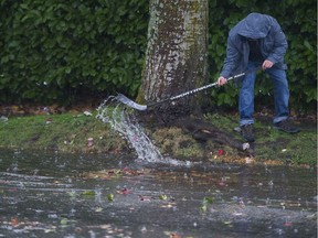 VANCOUVER, B.C.: October 18, 2017 – A man tries to clear a drain using a hockey stick on Victoria Drive in Vancouver on October 18 2017.