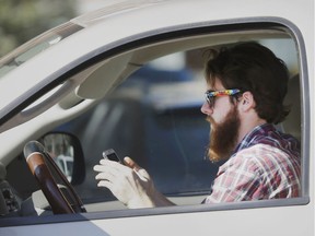 A man uses his cellphone while behind the wheel and trying to negotiate traffic. The B.C. government announced Monday it will designate distracted driving a ‘high-risk driving behaviour’ and hike fees on offenders, effective next March 1.