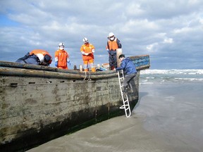Coast guard officers inspecting a battered wooden boat where eight bodies were found inside at a beach in Oga, Japan's Akita prefecture.