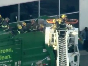 In this screenshot, fire crews rescue a man who was reportedly hiding in a dumpster outside a halfway house before getting stuck in a garbage truck.