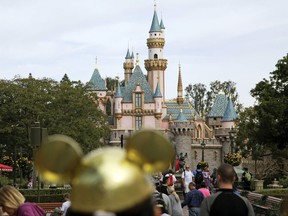 In this Jan. 22, 2015, file photo, visitors walk toward Sleeping Beauty's Castle in the background at Disneyland Resort in Anaheim, Calif.