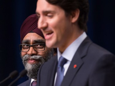 Defence Minister Harjit Sajjan, back, listens as Prime Minister Justin Trudeau responds to questions during a news conference at the 2017 United Nations Peacekeeping Defence Ministerial conference in Vancouver, B.C., on Wednesday November 15, 2017