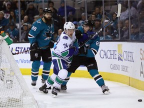 Reid Boucher of the Vancouver Canucks and Daniel O'Regan of San Jose battle for a loose puck behind the Sharks' net Thursday night in NHL action at the SAP Center in San Jose, Calif.