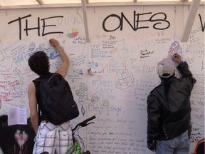 Two people sign a wall at 62 East Hastings Street in Vancouver on Tuesday, April 11, 2017. The wall, meant to be signed with wishes from friends and family to people who have died from drug use, was unveiled Tuesday as a memorial to the hundreds of people who have died during the opioid crisis.