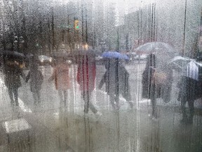Pedestrians carrying umbrellas to shield themselves from the rain are seen through a cafe window covered with rain and steam in Vancouver, B.C.