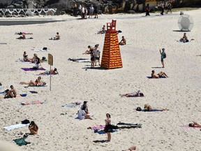 Beachgoers sunbathe next to a sculpture by artist Linton Meagher at the "Sculpture by the Sea" exhibition near Bondi beach in Sydney on October 19, 2017.