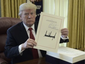 U.S. President Donald Trump holds up a document during an event to sign the tax cut and reform bill in the Oval Office at The White House in Washington, D.C., on Dec. 22, 2017.