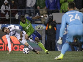 Vancouver Whitecaps defender Jake Nerwinski, left, tugs on the jersey of Sounders defender Nouhou as Whitecaps keeper Stefan Marinovic looks on during the MLS Western Conference semifinal on Nov. 2, 2017, in Seattle.
