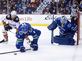 Chris Tanev defends against Andrew Cogliano as Canucks goalie Anders Nilsson looks on.