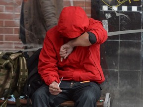 A man holds a needle after injecting himself at a bus shelter in Vancouver's Downtown Eastside.