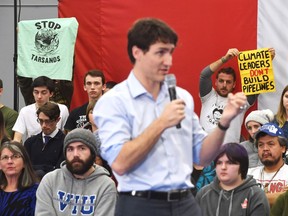 Protesters hold up signs as Prime Minister Justin Trudeau speaks at a raucous public town hall in Nanaimo on Vancouver Island, on Friday, Feb. 2, 2018.