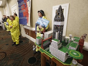 Ruchi Stair, of Seattle, and other demonstrators wear yellow suits intended to resemble gear worn by oil spill cleanup workers, Monday, March 5, 2018, as she stands next to a model of an offshore oil platform while attending a hearing in Olympia, Wash., organized by a coalition of environmental groups opposed to the Trump administration's proposal to expand offshore oil drilling off the Pacific Northwest coast. The hearing was held on the same day as an open house hosted by the federal Bureau of Ocean Energy Management.
