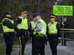 A man holds a sign behind RCMP officers watching protesters outside an entrance to Kinder Morgan's property in Burnaby, B.C., on Monday March 19, 2018.