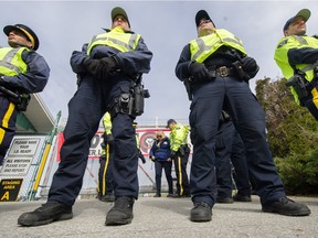 A line of police stand inside the five-metre no-go zone at the Kinder Morgan tank-farm gate as a protester is arrested against the gate.