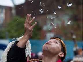Terry Azak, of the Nisga'a First Nation, blows feathers in the air while participating in a procession with a totem pole before it was raised in the Downtown Eastside of Vancouver, B.C., on Saturday November 5, 2016.