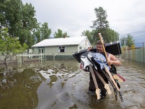Resident Lars Androsoff carries his friend's guitars as he walks through the floodwaters in Grand Forks, B.C., on Thursday, May 17, 2018.