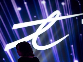 A woman is silhouetted as the Telus Corp. logo is displayed on a screen during a company event in Vancouver on October 2, 2015. Telus Corp. raised its dividend as it reported its first-quarter profit slipped lower compared with a year ago. The company says it will now pay make a quarterly payment to shareholders of 52.5 cents per share, up from 49.25 cents per share.