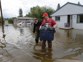 Homeowner Leo Lachance (left) and neighbour Sean Massey carry belongings from Lachance's house in Grand Forks, B.C., on Thursday, May 17, 2018.