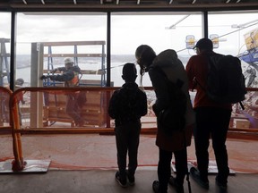 In this photo taken April 18, 2018, visitors to the Space Needle watch construction workers move large pieces of glass into position on the viewing platform of the structure in Seattle. The family-owned landmark is set to unveil the biggest renovation in its 56 year history next month, a $100 million investment in a single year of construction that transformed the structure's top viewing level some 500-feet above ground. The preservation and renovation project included the installation of floor-to-ceiling glass on the viewing deck, updated the structure's physical systems and adds a glass floor to the rotating restaurant.