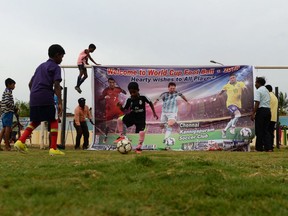 Indian kids play soccer beside a poster with an image of international star players (from left) Cristiano Ronaldo of Portugal, Lionel Messi of Argentina and Neymar Jr. of Brazil ahead of the FIFA 2018 World Cup in Russia.
