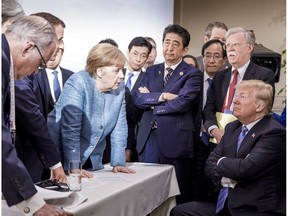 German Chancellor Angela Merkel speaks to U.S. President Donald Trump (seated right) while other political leaders watch on Saturday, June 9, 2018 at the G7 Leaders Summit in La Malbaie, Que.