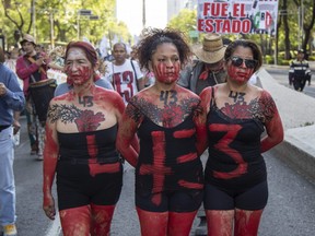 Three women painted with red paint to signify blood and the number 43, walk together during a protest to raise awareness of 43 students who went missing nearly four years ago, in Mexico City, Saturday, May 26, 2018.