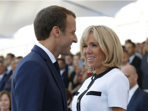 French President Emmanuel Macron takes his seat while his wife Brigitte Macron looks on before attending the traditional Bastille Day military parade on the Champs-Elysees avenue in Paris, France, Saturday, July 14, 2018.