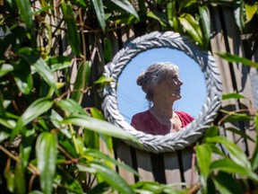 Marilyn Lenzen is reflected in a mirror on the fence in the backyard of her home as she poses for a photograph, in North Vancouver on Monday July 16, 2018. The largest-ever study to document symptoms of multiple sclerosis suggests patients had higher rates of certain conditions five years before they developed the first clinically recognizable signs of the disease.
