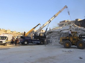 This photo provided by the Syrian Civil Defence White Helmets shows Syrian White Helmet civil defence workers with bulldozers working at the scene of an explosion that brought down a five-storey building in the village of Sarmada, near the Turkish border, on Sunday, Aug. 12, 2018.