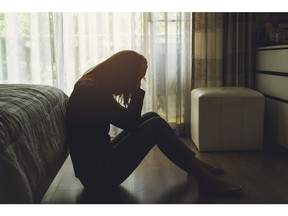 A depressed woman sitting head in hands in the dark bedroom.