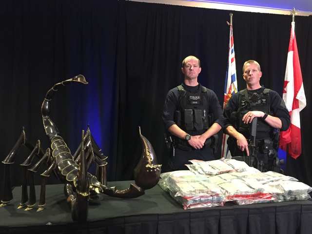Police officers with some of the spoils of crime, part of the items seized by police and displayed at a news conference on Friday, Aug. 10, 2018 in Vancouver that announced the arrest of 14 gangsters who face 93 charges.