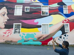 A man photographs a mural by David Ullock and Douglas Nhung at the Vancouver Mural Festival held in Mount Pleasant, Vancouver.