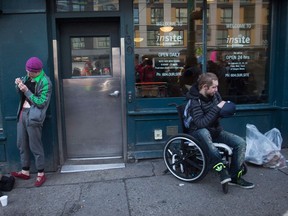 A woman, left, prepares to inject herself with an unknown substance as a man sits in a wheelchair outside Insite, the supervised consumption site, in the Downtown Eastside of Vancouver on February 21, 2017.