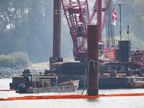 Workers stand on a small boat as a diver works below them after a tugboat capsized and sank on the Fraser River between Vancouver and Richmond, B.C., on Tuesday August 14, 2018.