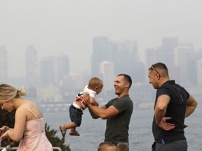 A man twirls a young child on a waterfront park as downtown Seattle disappears in a smoky haze behind, Sunday, Aug. 19, 2018. Poor air quality will be common across parts of the Pacific Northwest this week as winds push smoke from surrounding wildfires into the region, forecasters and regulators said. Air quality alerts are in effect for much of Washington state through Wednesday, according to the National Weather Service. The smoke is because of wildfires in British Columbia and the Cascade Mountains, according to the Puget Sound Clean Air Agency.