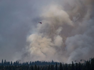A helicopter being used to fight a smaller fire nearby flies past a large plume of smoke rising from a wildfire near Fraser Lake, B.C., on Wednesday August 15, 2018. The British Columbia government has declared a provincial state of emergency to support the response to the more than 500 wildfires burning across the province.