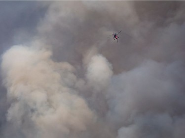 A helicopter being used to fight a smaller fire nearby flies past a large plume of smoke rising from a wildfire near Fraser Lake, B.C., on Wednesday August 15, 2018. The British Columbia government has declared a provincial state of emergency to support the response to the more than 500 wildfires burning across the province.