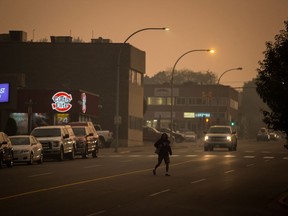 A woman walks across a street just after 10 a.m. in near darkness due to thick smoke blanketing the city because of wildfires in the region, in Prince George, B.C., on Friday, August 17, 2018.