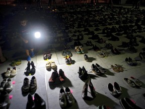 FILE - In this June 1, 2018 file photo, a child shines a light on hundreds of shoes at a memorial for those killed by Hurricane Maria, in front of the Puerto Rico Capitol in San Juan. Puerto Rico has conceded that Hurricane Maria killed more than 1,400 people on the island last year and not just the 64 in the official death toll.