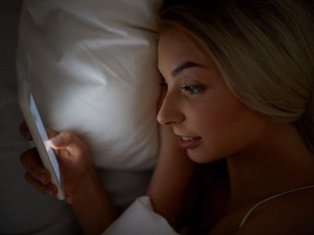 A young woman using her smartphone while in bed.