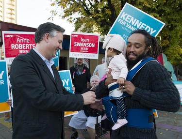 Independent candidate for mayor of Vancouver, Kennedy Stewart, helps get Amayra Clark back into her carrier after her father Kenya Clarke stopped to take a photo of his daughter and the candidate in Vancouver,  Oct. 20, 2018.