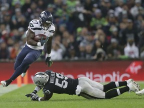 Seattle Seahawks running back Mike Davis (27), left, escapes the clutches of Oakland Raiders linebacker Tahir Whitehead (59) during the first half of an NFL football game at Wembley stadium in London, Sunday, Oct. 14, 2018.
