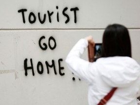 A tourist takes a picture of a tag reading "Tourists go home!" on her way to Guell Park in Barcelona on November 2, 2018.
