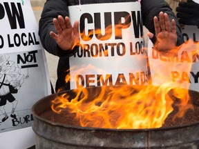 Striking Canada Post workers keep their hands warm as they picket at the South Central sorting facility in Toronto on Tuesday, November 13, 2018.