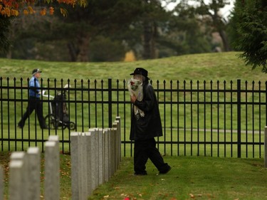 Don Kelles, 72, carries flowers to pay his respect to Gordon Cooper, a Juno beach engineer, and brother-in-law Sgt. Jack Martin as a golfer walks by during Remembrance Day ceremonies at God's Acre Veteran's Cemetery in Victoria on Sunday, November 11, 2018.