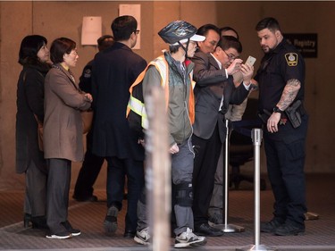 An unidentified man shows something on a smartphone to a sheriff while waiting to enter a courtroom to attend a bail hearing for Meng Wanzhou, the chief financial officer of Huawei Technologies, at B.C. Supreme Court in Vancouver, on  Dec. 7, 2018.