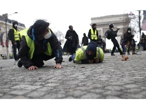 Demonstrators drop flat to the ground on the Champs-Elysees avenue during a protest Saturday, Dec. 8, 2018 in Paris. Crowds of yellow-vested protesters angry at President Emmanuel Macron and France's high taxes tried to converge on the presidential palace Saturday, some scuffling with police firing tear gas, amid exceptional security measures aimed at preventing a repeat of last week's rioting.